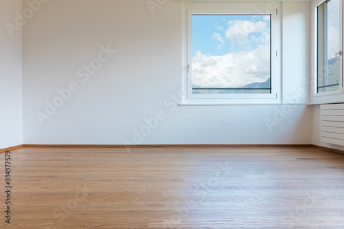 Frontal view of empty white room with parquet. Windows view on cluody sky
