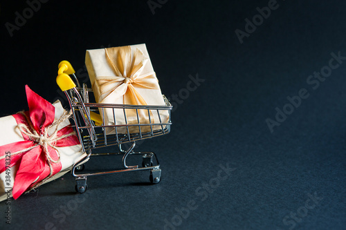 Box with a gift in Christmas packaging in a shopping cart on a black background. Black Friday, buying gifts for the new year. Space for text