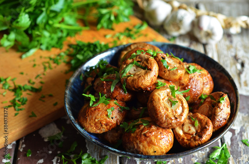 Grilled mushrooms with parsley in a blue bowl on a wooden background