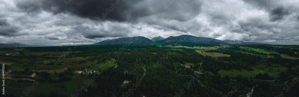 Luftaufnahme von Landschaft, Tal mit Bergen und Gebirge im Hintergrund bei dunklen Wolken