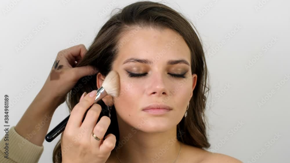 Attractive female face of a brunette well-groomed woman. Master applies makeup with a special brush in a beauty salon. Beauty industry of cosmetics backstage of professional makeup. Attractive female face of a brunette well-groomed woman. Master applies makeup with a special brush in a beauty salon. Beauty industry of cosmetics backstage of professional makeup.