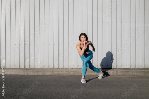 Portrait of sportswoman smiling outdoors in morning. Female in running outfit standing outdoors in city.