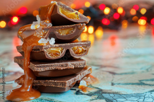 Macro chocolate pieces with caramel and sea salt against holiday background and dried oranges