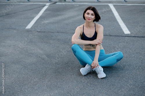 Fit young woman sitting outdoors after workout session in morning. Female fitness model relaxing and staring at camera.