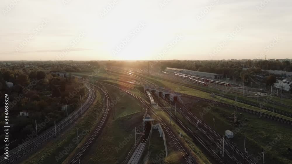 Trains passenger transport moving forward on railways at meadow sunset and camera from drone moves with one of city trains. Trains passenger transport moving forward on railways at meadow sunset and camera from drone moves with one of city trains.