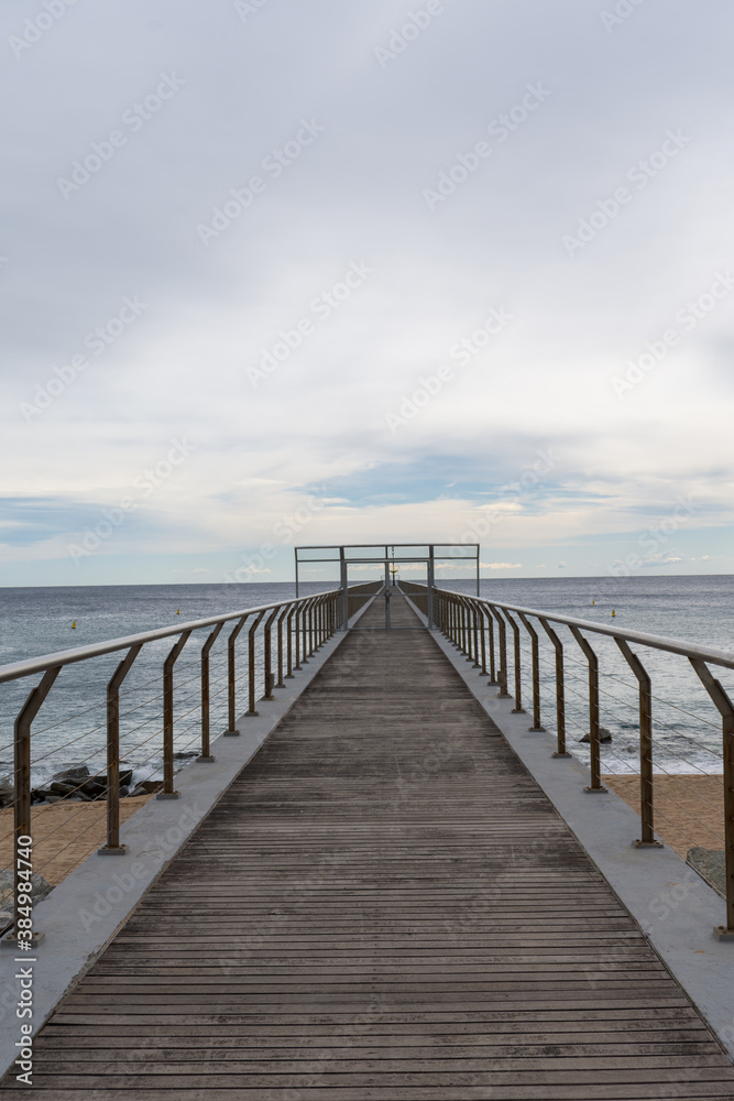 Perspective of footbridge over beach and sea, a cloudy day, in Badalona, Catalonia, Spain, in vertical