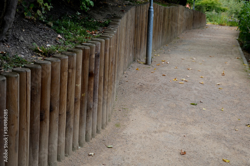 the park threshing beige gravel roads in the sloping terrain have on one side a wooden palisade retaining wall that holds the soil the slope. grows lots of blue yellow flowers gardener watered