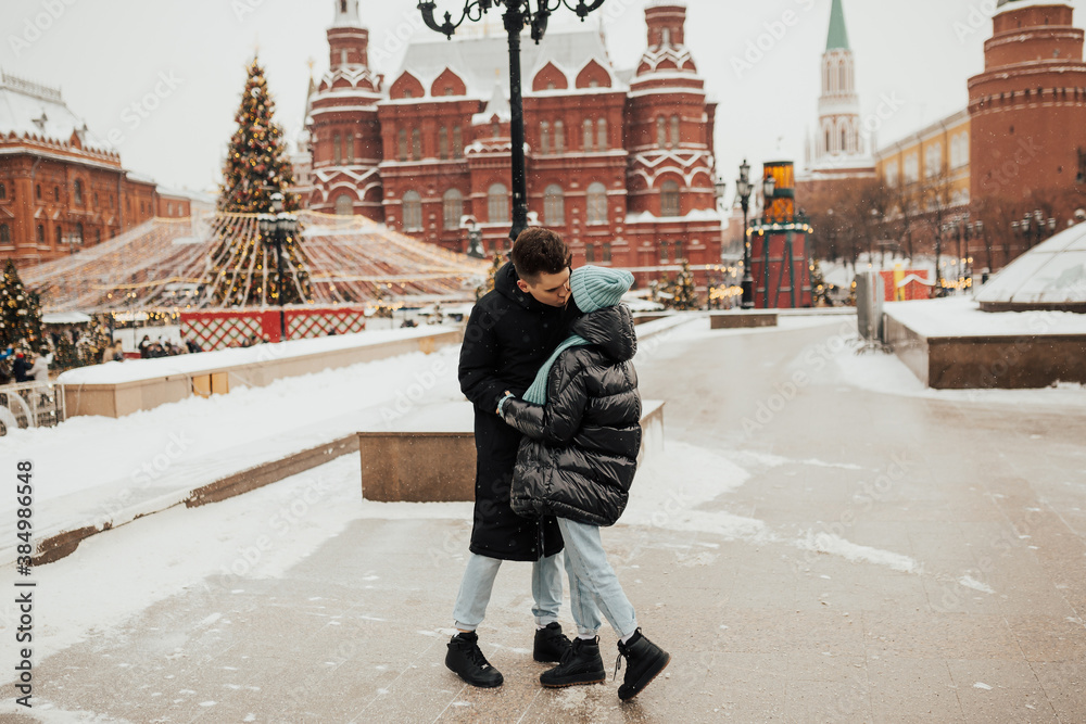 Happy young beautiful couple in love. They hugging and kissing outdoors in winter city. They travel around Russia.