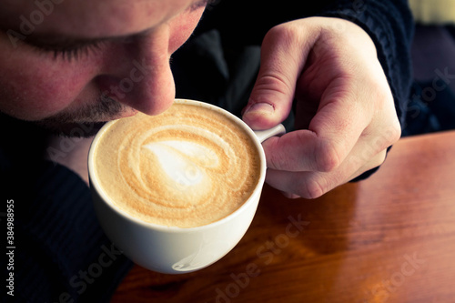 A man tries delicious coffee in a cafe. Heart in a coffee Cup.