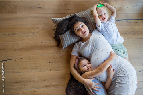Top view of pregnant woman with small children indoors at home, lying on floor.