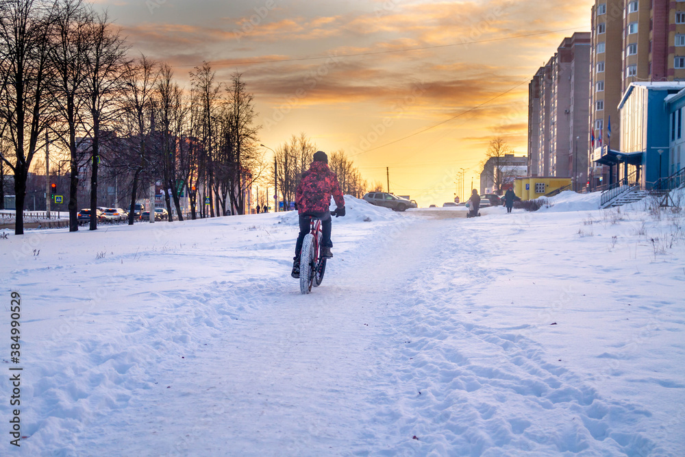 A man rides a Bicycle through the snow in winter. Sunset. Street in the city.