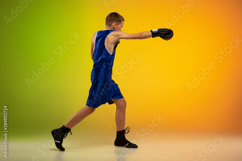 Fighter. Teenage professional boxer training in action, motion isolated on gradient background in neon light. Kicking, boxing. Concept of sport, movement, energy and dynamic, healthy lifestyle. © master1305
