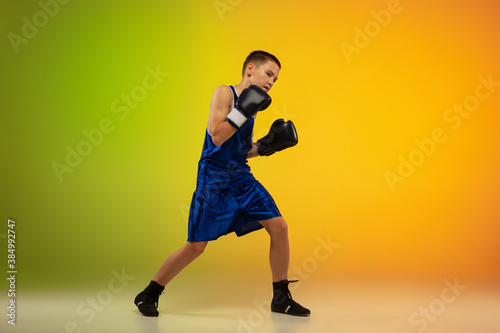 Stronger. Teenage professional boxer training in action, motion isolated on gradient background in neon light. Kicking, boxing. Concept of sport, movement, energy and dynamic, healthy lifestyle. © master1305