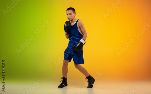 Champion. Teenage professional boxer training in action, motion isolated on gradient background in neon light. Kicking, boxing. Concept of sport, movement, energy and dynamic, healthy lifestyle. © master1305