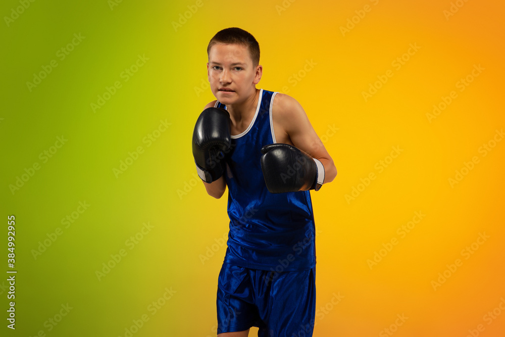 Emotions. Teenage professional boxer training in action, motion isolated on gradient background in neon light. Kicking, boxing. Concept of sport, movement, energy and dynamic, healthy lifestyle.