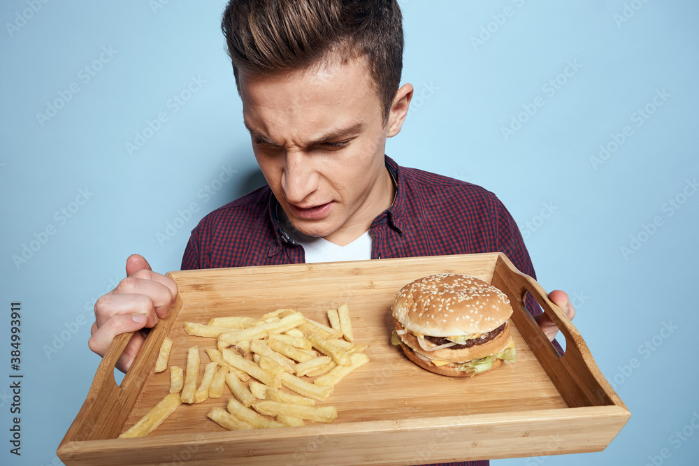 Man with wooden pallet fast food french fries hamburger hunger diet food blue background Man with wooden pallet fast food french fries hamburger hunger diet food blue background