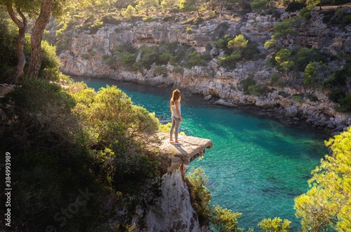 Canvas Print Girl standing on a ledge over the sea in beautiful soft sunlight, Cala Pi, Mallo