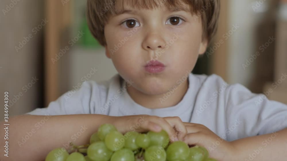 Child Eat Sweet Grape. Little Boy Vegetarian is Eating White Grapes From Plate Sitting Home at Table in Kitchen. Healthy Organic Vegetarian Food. Fruit harvest. Child Eat Sweet Grape. Little Boy Vegetarian is Eating White Grapes From Plate Sitting Home at Table in Kitchen. Healthy Organic Vegetarian Food. Fruit harvest.