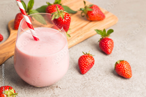 Glass of fresh strawberry milkshake, smoothie and fresh strawberries on pink, white and wooden background. Healthy food and drink concept.