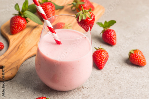 Glass of fresh strawberry milkshake, smoothie and fresh strawberries on pink, white and wooden background. Healthy food and drink concept.