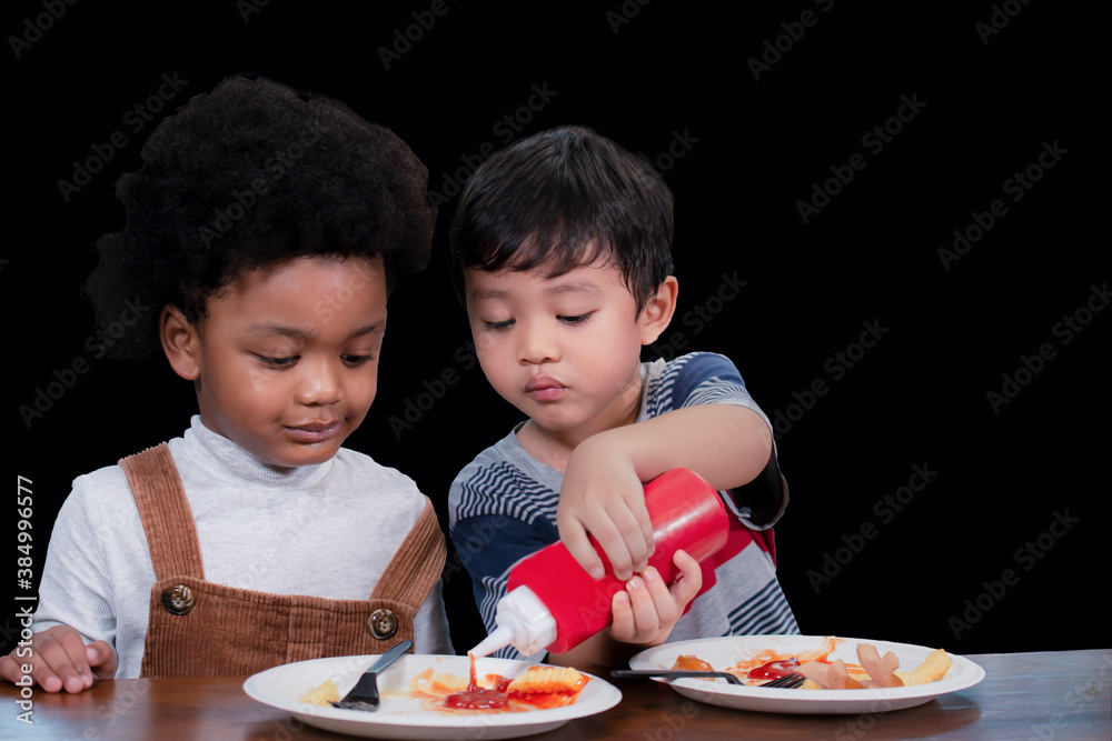 Portrait of little cute black boy and asian boy eating french fries potato with ketchup in the cafe. African American kid and white kid enjoy eating french fries. Happy child eating unhealthy food. Portrait of little cute black boy and asian boy eating french fries potato with ketchup in the cafe. African American kid and white kid enjoy eating french fries. Happy child eating unhealthy food.