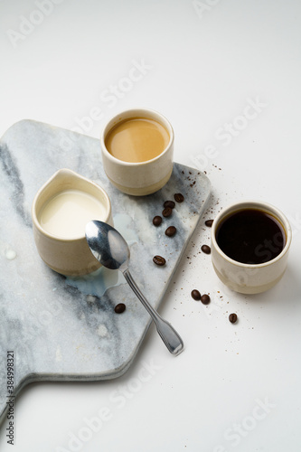 Coffee and milk in ceramic cups with beans, marble