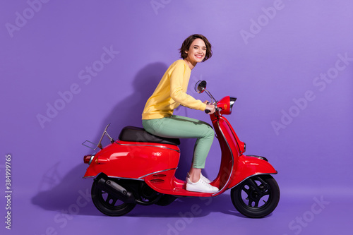 Full length body size profile photo of brunette pretty student driving retro red moped smiling happily isolated on bright purple color background