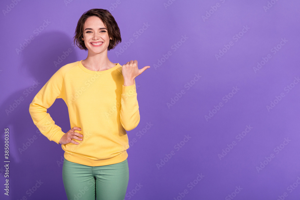 Photo of positive girl point thumb finger empty space for ads promotion wear trousers pullover isolated on violet color background Photo of positive girl point thumb finger empty space for ads promotion wear trousers pullover isolated on violet color background