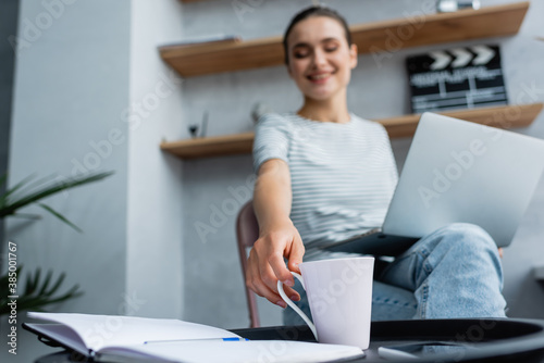 Foto Selective focus of woman with laptop taking cup near open notebook on coffee tab