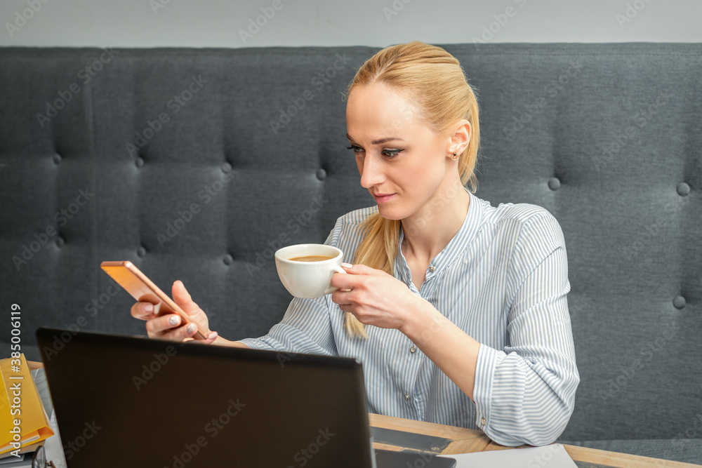 Young caucasian businesswoman with smartphone and cup of coffee working at home office