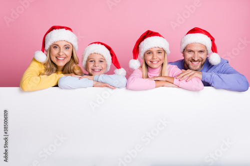 Photo of family mom mommy dad daddy little kids wear santa claus hat put hands on white board isolated over pastel color background