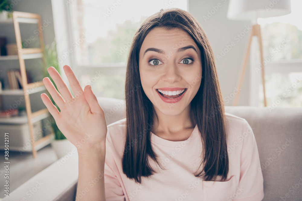 Photo portrait of young woman waving saying hi sitting on sofa indoors