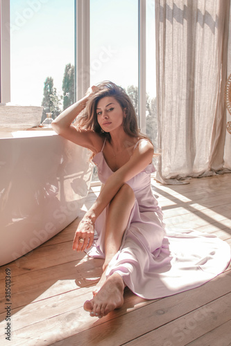 young glamour girl is sitting near white bath near window in the boho style bathroom background in sun lights, morning lifestyle concept, free space 