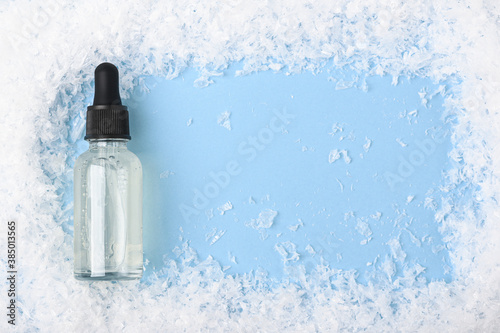 Serum in a transparent glass bottle with a pipette on a blue background with snow. Moisturizing skincare product in the winter season. Beauty product for face, hand, body skin care. Copy space