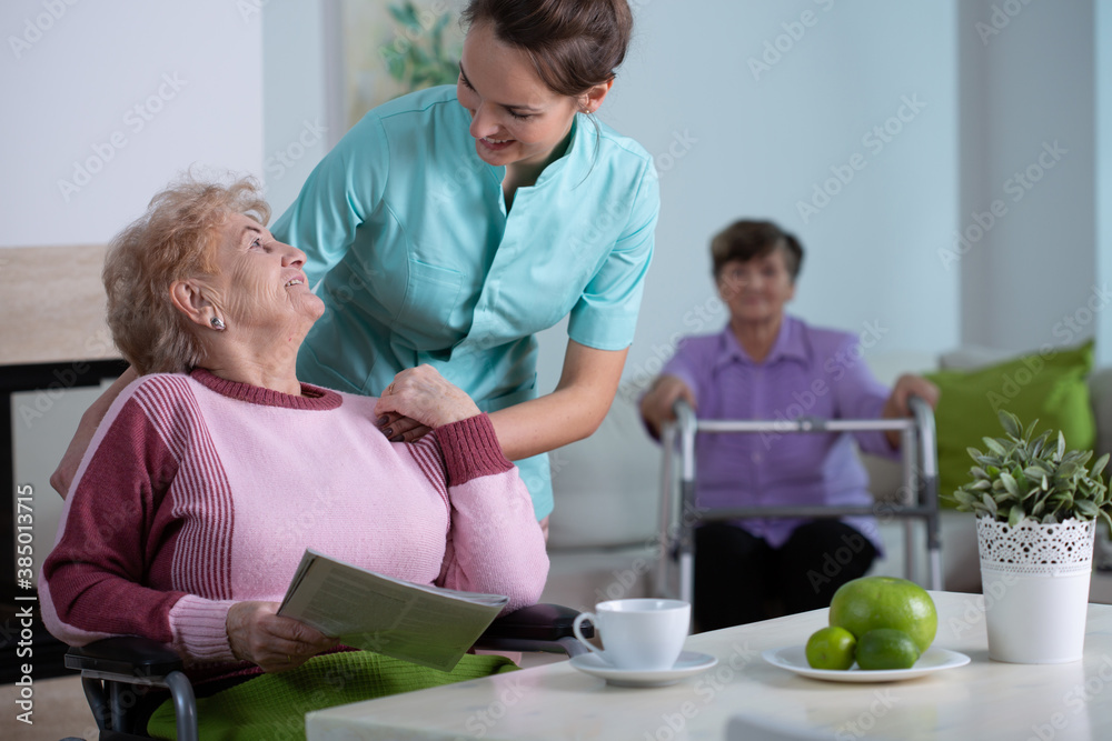 Female senior residents in living room of nursing facility with supporting nurse Female senior residents in living room of nursing facility with supporting nurse