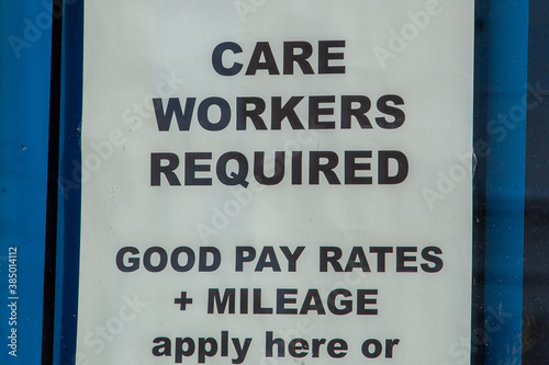 A sign advertising a job in a window stating that care workers are required