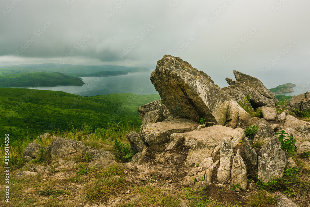 Bay of the sea and large rocks from the hilltop of the mountainous coast, summer landscape and seascape in cloudy cloudy weather.