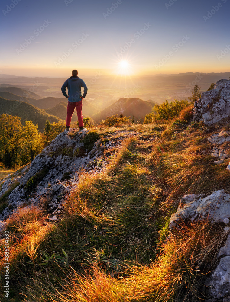 Fototapeta premium Back view silhouette of young tourist traveler man standing with beautiful morning sunrise of mountain landscape