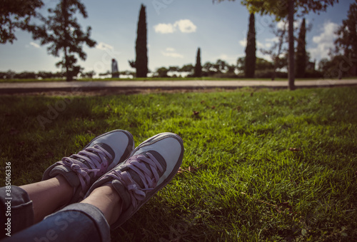Piernas de mujer vistiendo jeans y zapatillas clásicas mientras yace sobre el césped del parque público Juan Carlos I
 photo