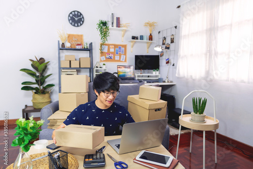 Young Asian man business owner working at home Start up for Business Online, working with laptop for checking, packaging delivery online market on purchase orders to customer, e-commerce concept.