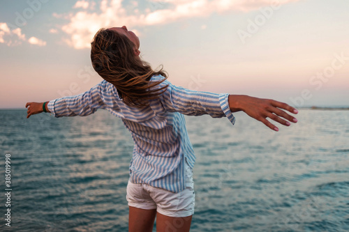 Woman enjoying freedom. Standing arms outstretched back and enjoy life on the beach at sea under sunlight sky.