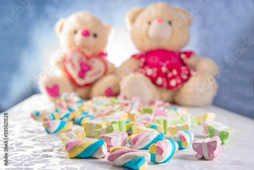 Colorful marshmallows in detail and defocused teddy bears in the background, blue gradient background, selective focus. © Milton Buzon