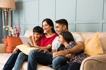 Indian family using smartphone, laptop or tablet, watching movie, surfing internet, sitting on sofa
