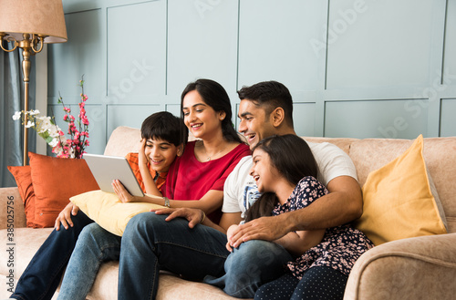 Fotografie Indian family using smartphone, laptop or tablet, watching movie, surfing intern