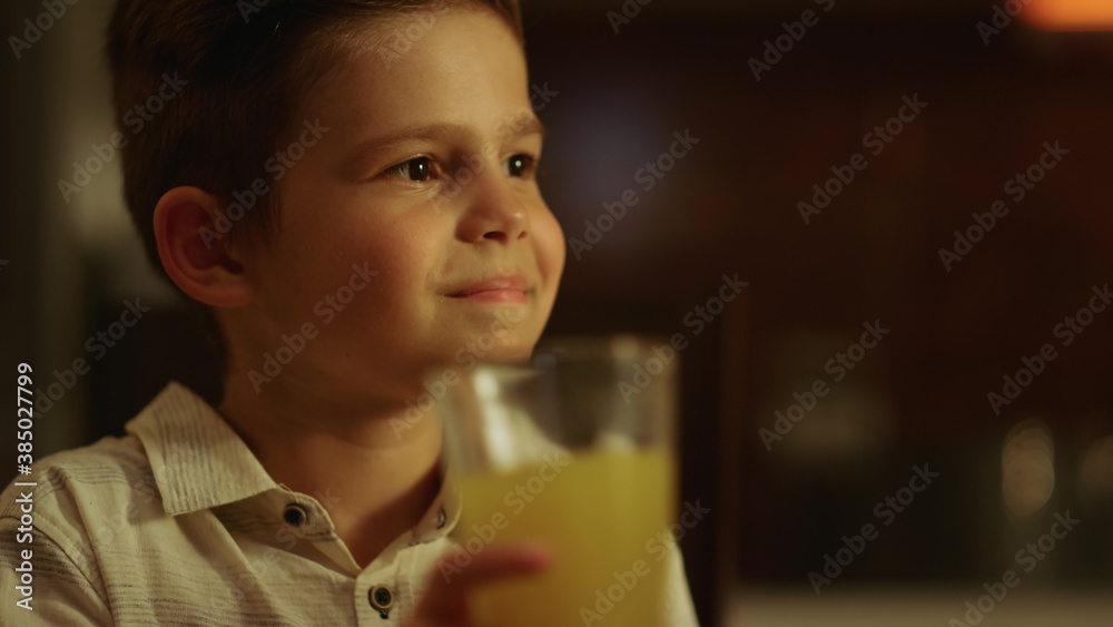 Boy sitting at dining table. Smiling child holding glass of juice in hand Boy sitting at dining table. Smiling child holding glass of juice in hand