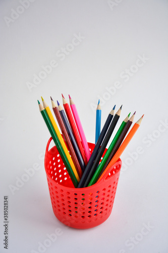 Colored sharpened pencils for drawing in a red pencil holder close-up on a light background