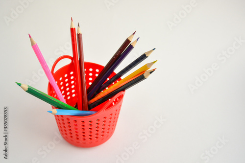 Colored sharpened pencils for drawing in a red pencil holder close-up on a light background