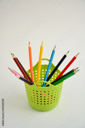 Colored sharpened pencils for drawing in a green pencil holder close-up on a light background