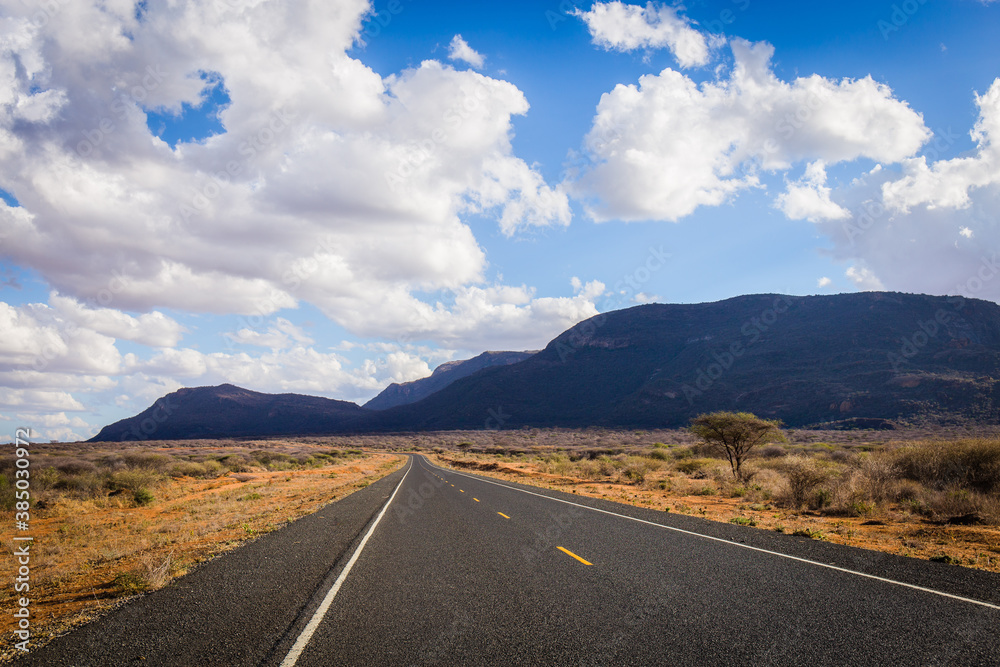 Kenya road in national park, mountains, clouds