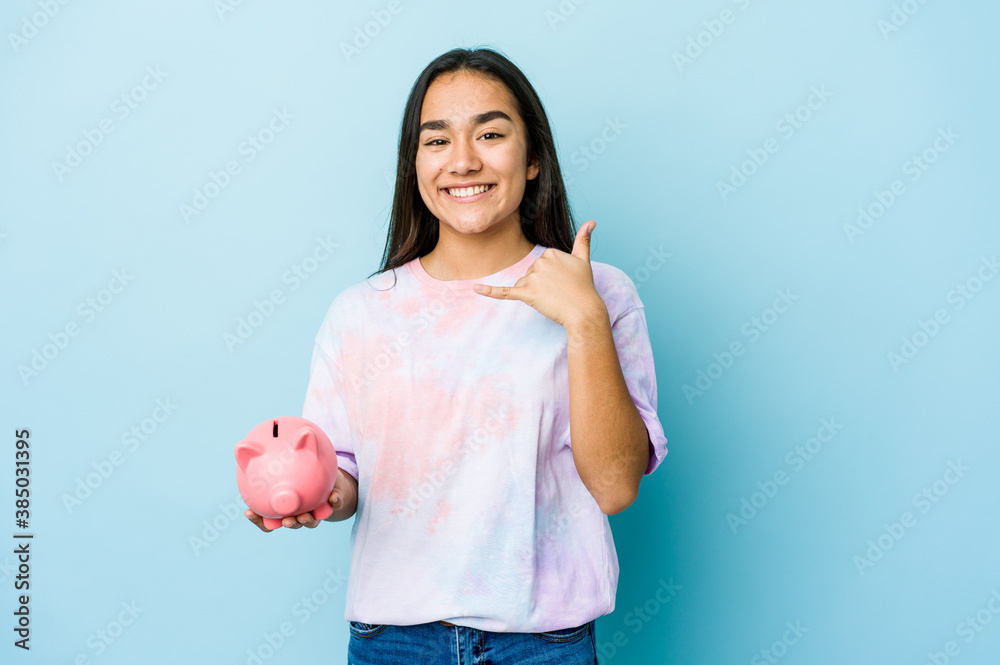 Young asian woman holding a pink bank over isolated background showing a mobile phone call gesture with fingers. Young asian woman holding a pink bank over isolated background showing a mobile phone call gesture with fingers.